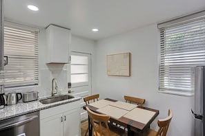Cocina compacta con pileta, estufa y zona de comedor con sillas.