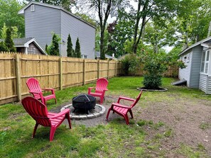 A backyard with a fire pit, four red Adirondack chairs, a wooden fence, and a small tree. - Spacious & Private 1 BR Home 0.8 Miles to Beach (Old Orchard Beach)