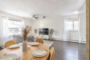 A modern living room with a dining area, a flat-screen TV, and a ceiling fan.