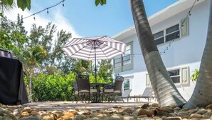 Une terrasse extérieure avec une table et des chaises, un parasol à rayures et un bâtiment en arrière-plan.