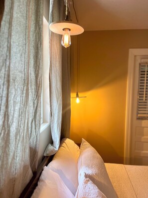 Ein Zimmer mit Bett, Vorhängen, einer Pendelleuchte und einem Fenster.
