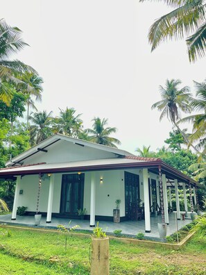 A single-story house with a covered porch, surrounded by lush greenery and palm trees. - Peaceful private villa just steps from the beach in Habaraduwa (Habaraduwa)