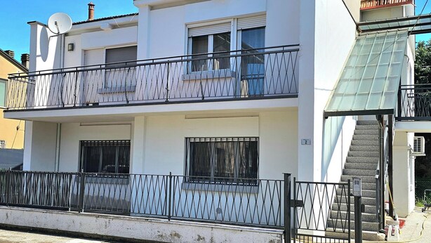 Ein zweistöckiges Gebäude mit Balkon, Treppe und Satellitenschüssel.