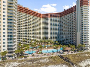 Un hotel moderno de gran altura con varios balcones, un área de piscina con palmeras y vistas a la playa.