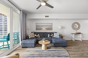 A modern living room with a sectional sofa, a round coffee table, and a view of the ocean through large windows. - 3bd Beachfront Resort Condo| Pools, Hot Tubs & Views (Panama City Beach)