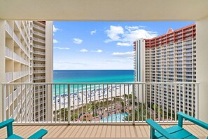 Ein Balkon mit Blick auf Strand und Meer, ein Poolbereich sowie angrenzende Hochhäuser.