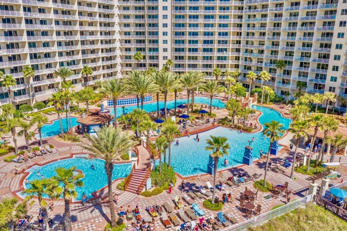 A hotel with multiple swimming pools, palm trees, and sun loungers.