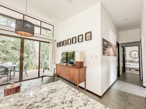 A modern living room with a large TV, wooden cabinet, and a dining area with a marble table.