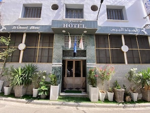 Fachada de hotel con un letrero que dice 'HOTEL', una entrada amplia y plantas en macetas.