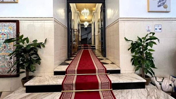 A hotel lobby with a marble staircase, red carpet, potted plants, and artwork on the walls.