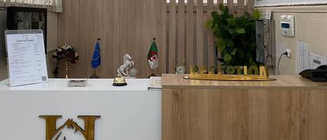 A reception desk with a wooden backdrop, a sign for Hotel Le Chaval Blanc, and a flag of Monaco.