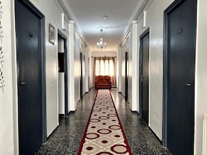 Ein Hotelgang mit Teppichmuster, dunklen Türen und einem Kronleuchter.