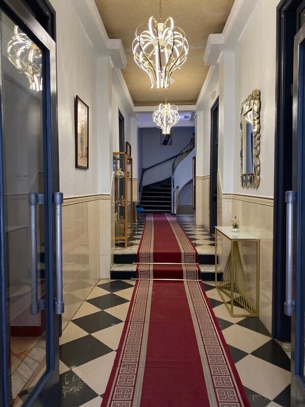 Un pasillo con piso a cuadros, alfombra roja y una escalera.