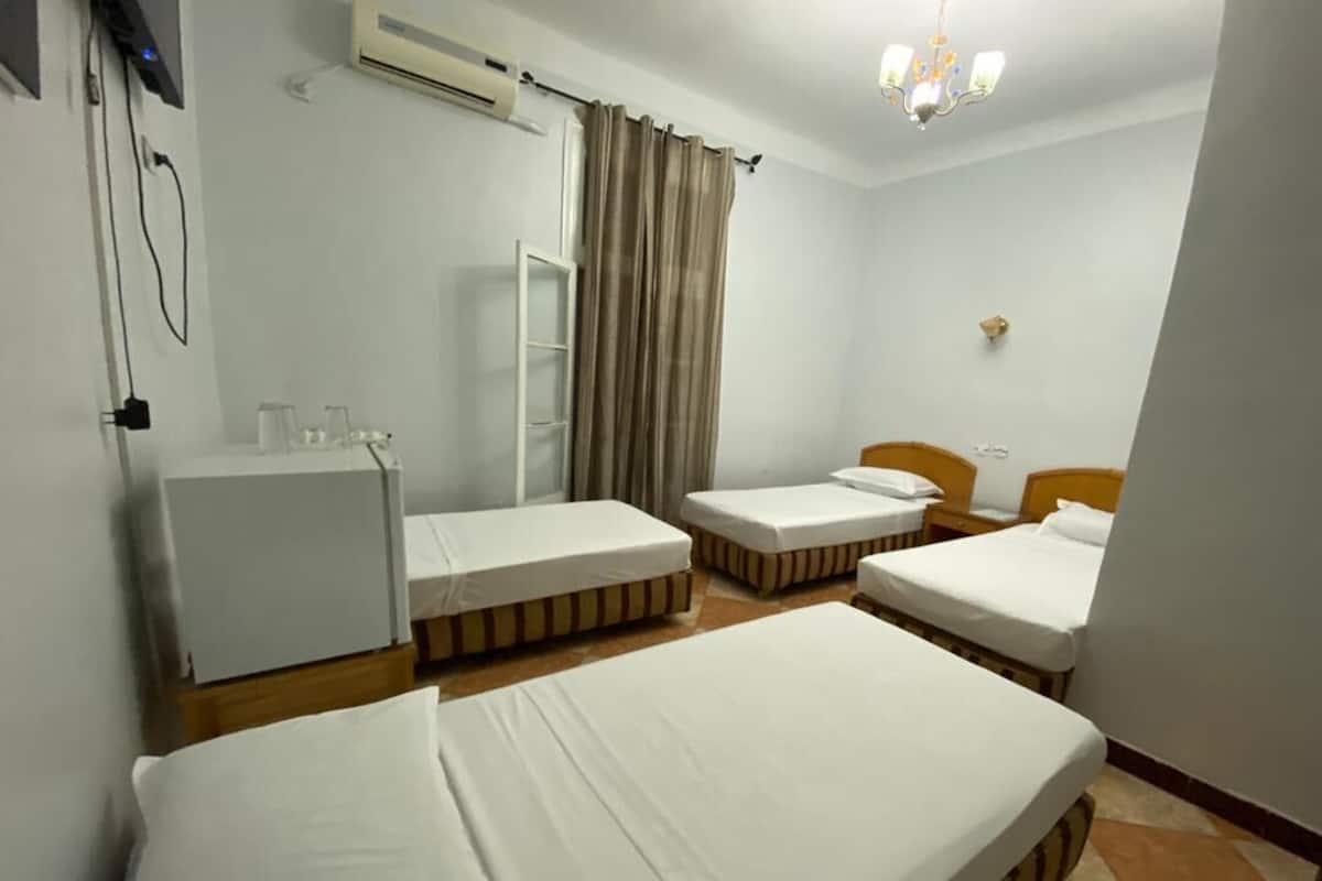 A hotel room with three single beds, a small desk, a chair, a wardrobe, and an air conditioning unit.