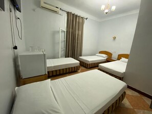 Habitación de hotel con tres camas individuales, un escritorio pequeño, una silla, un armario y un equipo de aire acondicionado.