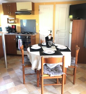 Ein Essbereich mit Tisch für vier Personen, eine Küche mit Herd und Backofen sowie ein an der Wand montierter Fernseher.