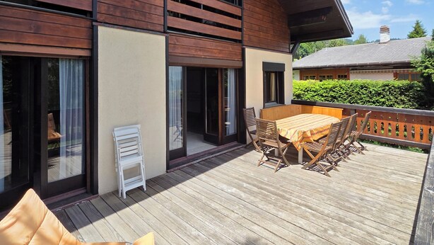 A modern house with a wooden deck, large windows, and a dining area with outdoor furniture. - Fully-equipped family chalet with large garden 300m from lifts. (Leysin)