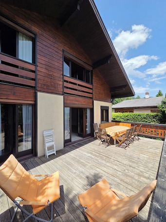 A modern house with a wooden deck, large windows, and a dining area with outdoor furniture.. Fully-equipped family chalet with large garden 300m from lifts.