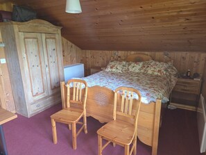 Une pièce en bois comprenant un lit, deux chaises en bois, un bureau et une armoire.
