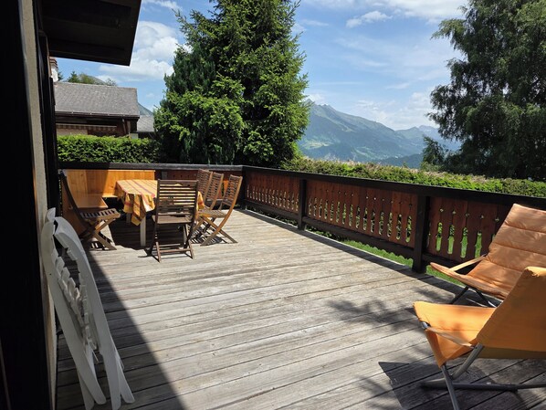 A wooden deck with a table and chairs, overlooking a mountainous landscape.