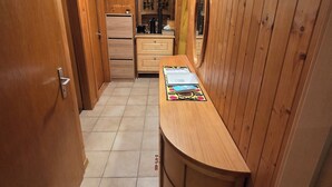 A narrow hallway with wooden walls and a tiled floor, leading to a kitchen area with a refrigerator, a sink, and a countertop with a mirror. - Fully-equipped family chalet with large garden 300m from lifts. (Leysin)