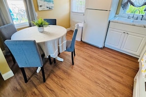 A compact kitchen with a round table, chairs, a refrigerator, and a window with a view of greenery.