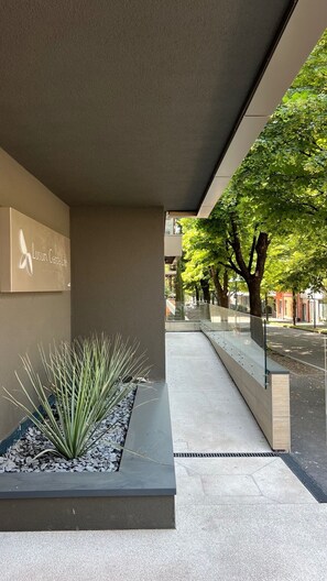 Ein moderner Gebäudeeingang mit einem Schild für 'Luxur Garden Life', einer Glasreling und einem Weg, der zu einer von Bäumen gesäumten Straße führt.