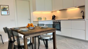 A modern kitchen with white cabinets, a built-in oven, and a dining area with a wooden table and chairs.