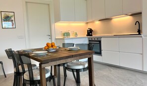 Eine moderne Küche mit weißen Schränken, einem eingebauten Backofen und einem Essbereich mit einem Holztisch und Stühlen.