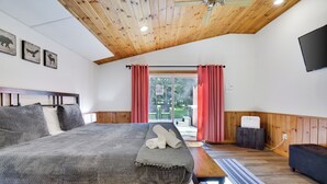 A bedroom with a bed, wooden ceiling, a flat-screen TV, and a window with curtains.