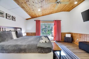 A bedroom with a bed, wooden ceiling, a flat-screen TV, and a window with curtains. - Poconos Lake Cabin Retreat - Hot Tub, Sauna, Movie & Game Room (Albrightsville)