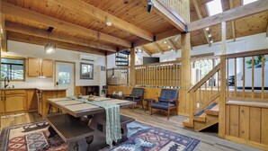 A spacious room with a wooden ceiling, a dining table, chairs, a staircase, and a view of the outdoors.