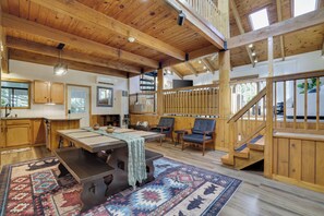 A spacious room with a wooden ceiling, a dining table, chairs, a staircase, and a view of the outdoors. - Poconos Lake Cabin Retreat - Hot Tub, Sauna, Movie & Game Room (Albrightsville)