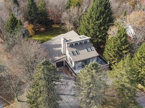 Uma casa moderna de dois andares com telhado inclinado, rodeada por uma floresta densa.