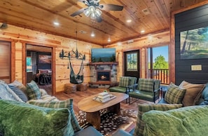 A cozy cabin interior with a fireplace, wooden walls, and a large window. - Amazing BRAND NEW 8bdrm Cabin-Pool-Arcades-Gazebo (Sevierville)