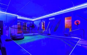 A blue-lit indoor swimming pool with a netted area, a lifebuoy, and a staircase. - Amazing BRAND NEW 8bdrm Cabin-Pool-Arcades-Gazebo (Sevierville)