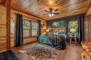 A log cabin bedroom with a bed, a ceiling fan, a fur rug, and a window with curtains. - Amazing BRAND NEW 8bdrm Cabin-Pool-Arcades-Gazebo (Sevierville)