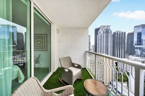 A balcony with a wicker chair, a small table, and a view of tall buildings. - Luxury executive Studio in Brickell (Miami)