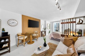 Een moderne woonkamer met een televisie, een klok, een houten wandpaneel, een bank, een salontafel en een bed.