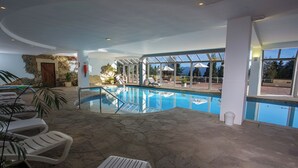 An indoor swimming pool with clear glass walls, lounge chairs, and a stone floor. - Lake View Quadruple Stay with Free Breakfast, Spa & Wellness Center (San Carlos de Bariloche)