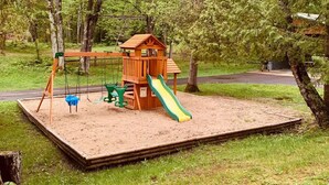 Un espace de jeux avec des balançoires, un toboggan et une structure d’escalade, situé dans un parc.