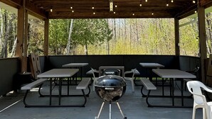 Un espace extérieur abrité avec un barbecue, des tables de pique-nique et des bancs.