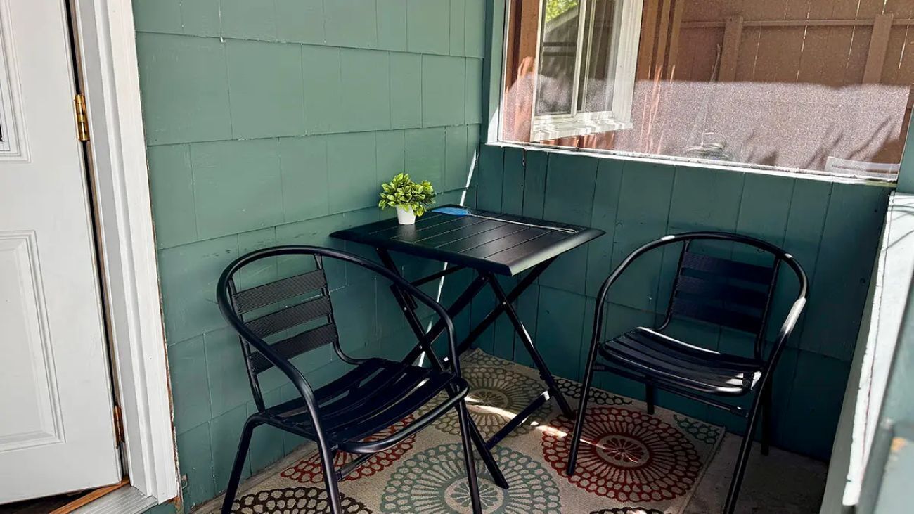 A small outdoor seating area with two chairs and a table, a potted plant, and a patterned rug.