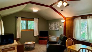 Un salon chaleureux avec un ventilateur de plafond, un téléviseur, une cheminée et un coin repas.