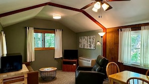 A cozy living room with a ceiling fan, a television, a fireplace, and a dining area.