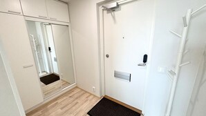 Un couloir doté d’un plancher en bois, d’une porte blanche avec un judas, d’un porte-manteau et d’un miroir qui reflète le couloir.