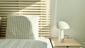 Un lit avec un oreiller à texture, une lampe de chevet et des stores horizontaux.