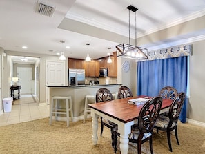 A dining area with a wooden table and chairs, a kitchen in the background, and a blue curtain. - Reunion Elegant Disney Condo, Resort Amenities (Kissimmee)