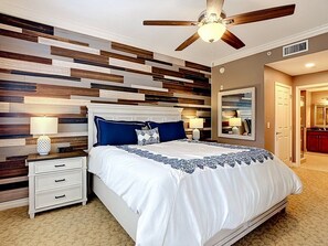 Ein Schlafzimmer mit modernem Design, ausgestattet mit einem Bett, das eine weiße und blaue Bettdecke und ein Holz-Kopfstück sowie einen Deckenventilator hat.