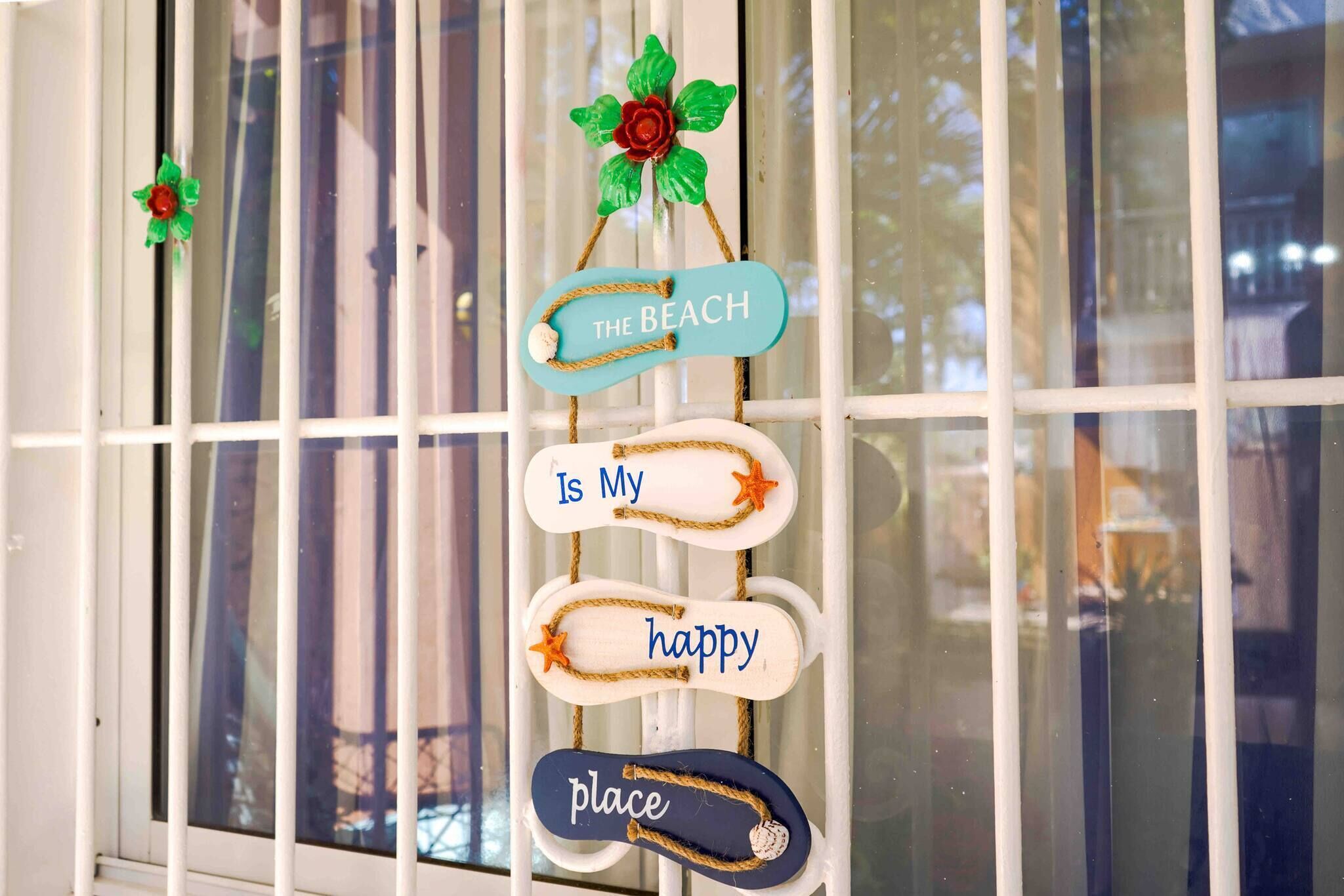 A window with decorative signs saying 'The Beach Is My Happy Place' and a flower decoration.